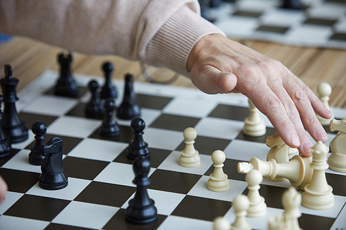 Wrinkled hand of old chess player getting opponent chess figure after making successful chess move