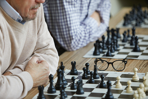 Two serious chess players sitting in row with crossed hands during difficult chess tournament