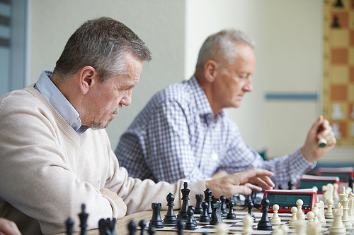 Two aged chess players with grey hair playing next to each other at amateur chess tournament