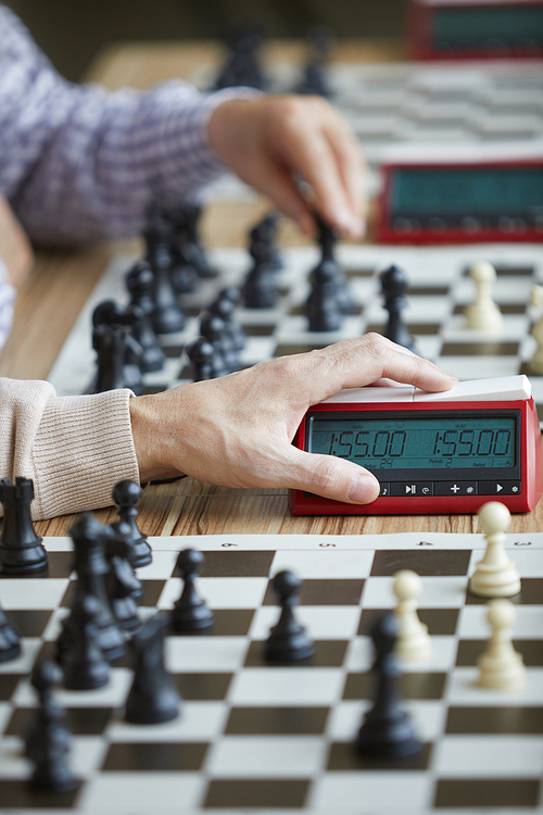 Wrinkled hand of aged experienced grandmaster in beige sweater gently pressing chess clock