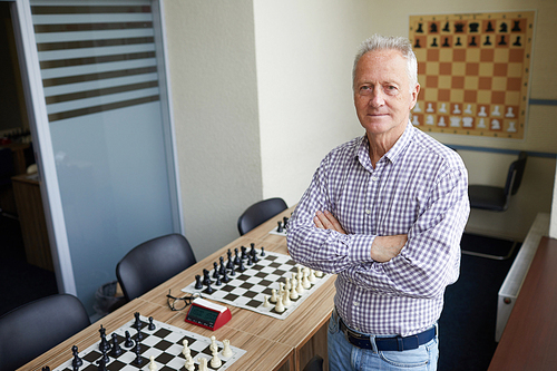 Aged male teacher at chess club posing for pictures for advertising chess classes for schoolchildren