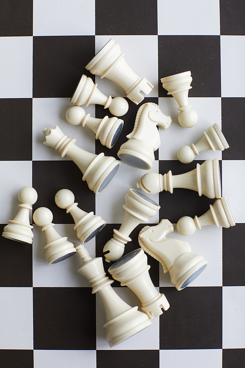 Randomly scattered lying white wooden chess pieces in center of black and white chess board