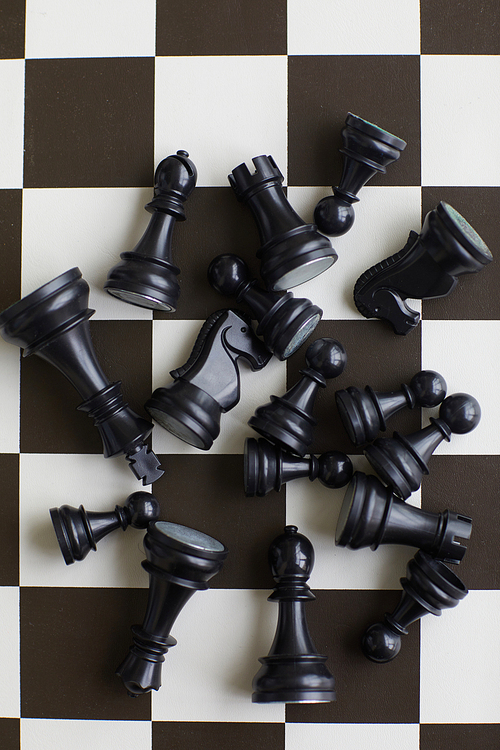 Randomly scattered lying black wooden chess pieces in center of black and white chess board