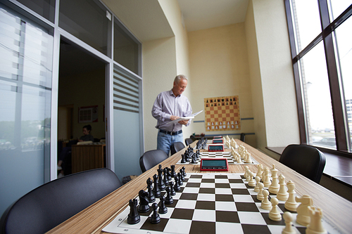 Aged male teacher in shirt checking how well prepared classroom is before next chess class