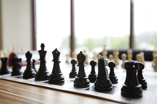 Arranged wooden chess pieces standing in perfect order on table in front of window in classroom of chess club