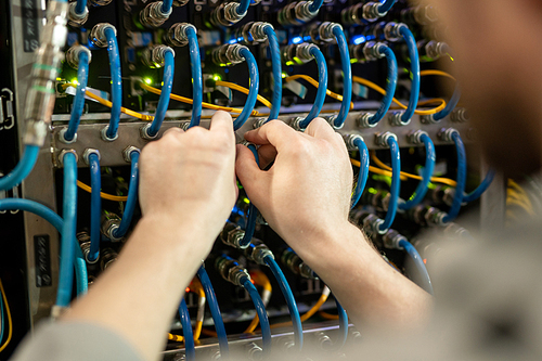 Close-up of unrecognizable server support specialist checking cables of switchboard while examining server, copy space
