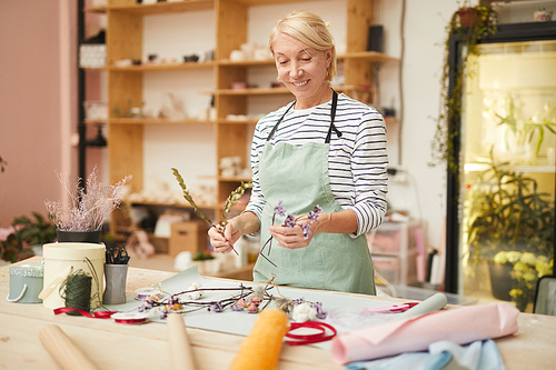 Waist up portrait of smiling mature woman creating flower compositions in art studio, copy space