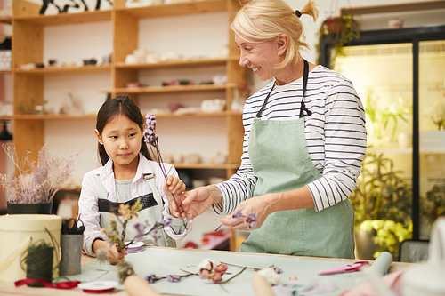 Portrait of smiling mature woman creating flower compositions with little Asian girl, copy space