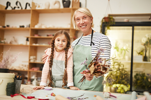 Waist up portrait of smiling mature woman  while creating flower compositions with cute girl in art studio, copy space