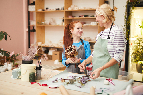 Waist up portrait of smiling mature woman creating flower compositions with teenage girl in art studio, copy space