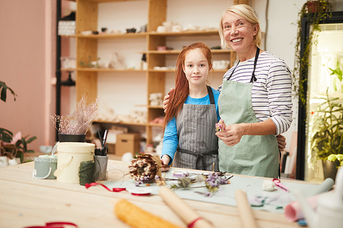 Waist up portrait of smiling mature woman  while creating flower compositions with teenage girl in art studio, copy space