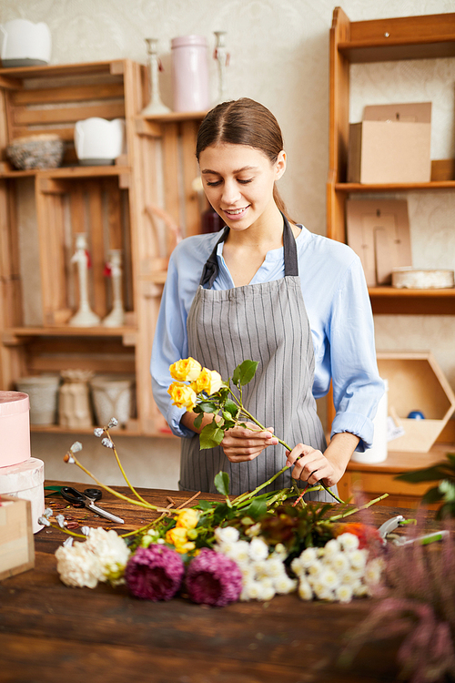 Waist up portrait of smiling young woman arranging flowers in flower shop