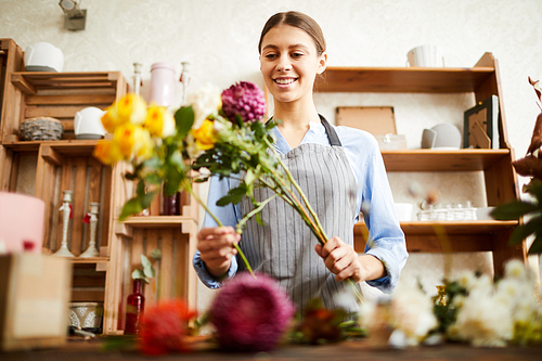 Low angle portrait of smiling young woman arranging bouquets while working in flower shop, copy space
