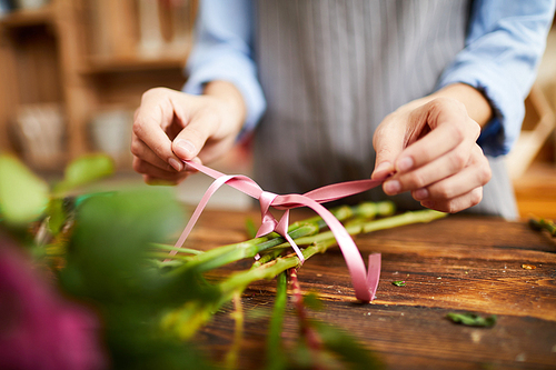 Close up of female florist tying ribbon on bouquet while arranging compositions in flower shop, copy space