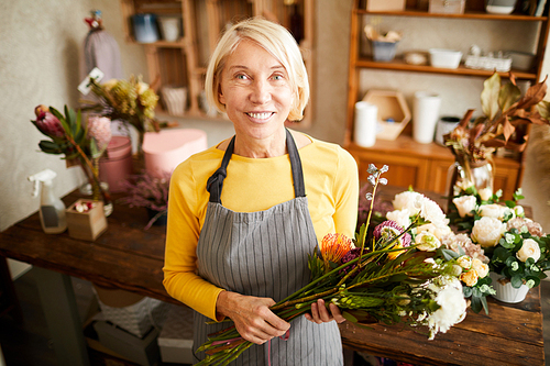 Waist up portrait of mature female florist holding bouquet and   while working in flower shop, copy space