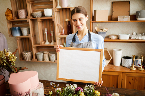 Waist up portrait of young female florist holding whiteboard and   while working in flower shop, copy space