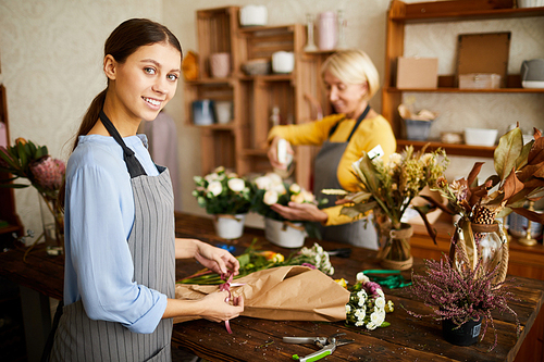 Portrait of smiling female florist cutting flower stems while arranging bouquets in flower shop, copy space