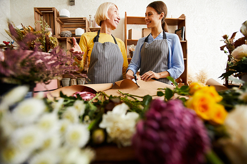 Low angle portrait of two florists smiling to each other while working in flower shop, copy space