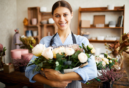Waist up portrait of smiling florist holding bouquet of roses while posing in flower shop