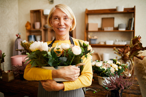 Waist up portrait of mature florist holding bouquet of roses while posing in flower shop