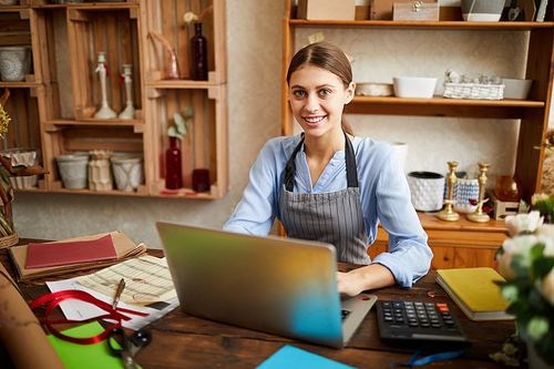 Portrait of female small business owner using laptop and  in shop, copy space