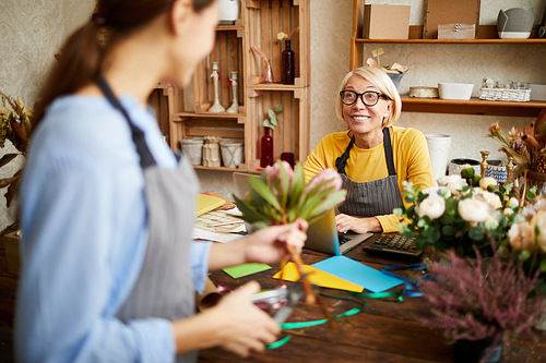 Portrait of mature flower shop owner talking to florist and smiling, copy space