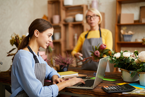 Side view portrait of smiling female small business owner using laptop in flower shop, copy space