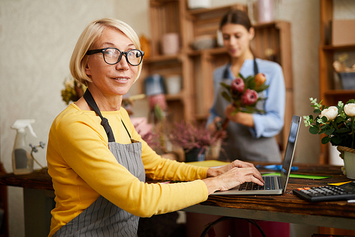 Side view portrait of mature female small business owner using laptop and  in flower shop, copy space