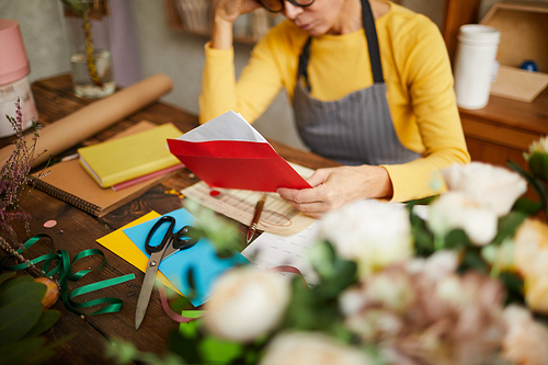 Portrait of small business owner holding red envelope while doing accounting in flower shop, copy space