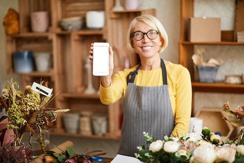 Waist up portrait of mature female florist holding smartphone with blank screen presenting mobile app, copy space
