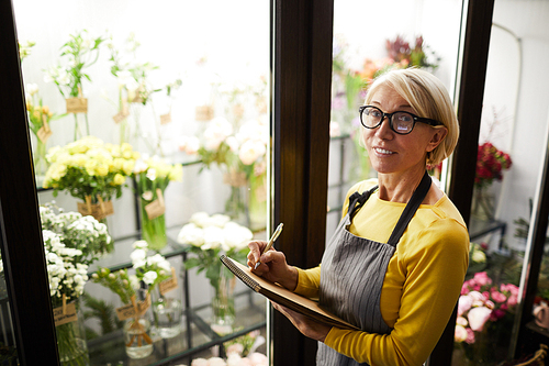 Waist up portrait of mature female florist holding clipboard  standing by glass display, copy space