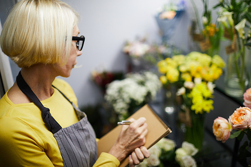 Portrait of mature female florist holding clipboard looking flowers in display, copy space