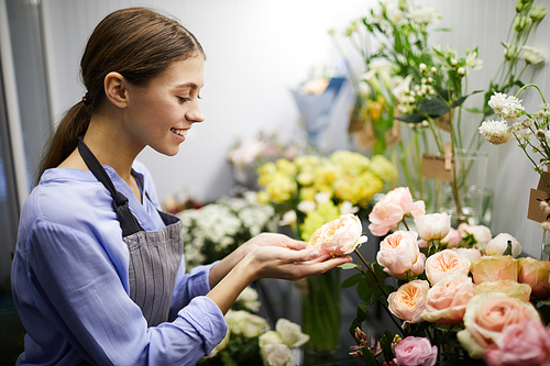 Waist up portrait of smiling female florist looking at flowers in glass display, copy space