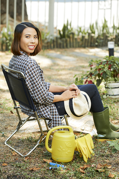 Portrait of cheerful young female gardener resting on chair in backyard