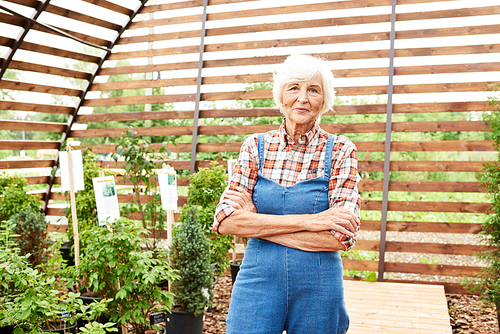 Portrait of happy senior woman posing in garden standing with arms crossed and , copy space