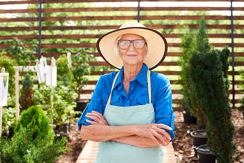 Waist up portrait of happy senior woman posing in garden standing with arms crossed, copy space