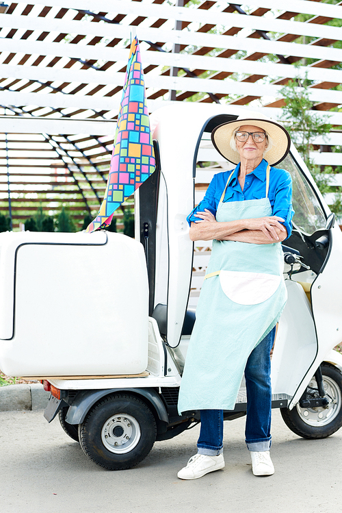 Full length portrait of senior woman posing in garden standing next to moving cart with arms crossed
