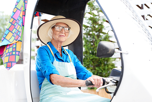 Portrait of cheerful senior woman driving bicycle car in garden or plantation, copy space