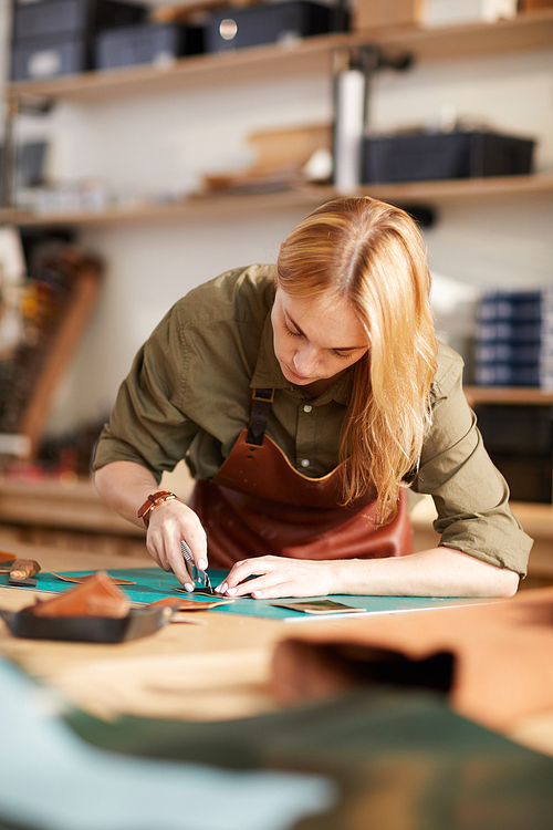 Warm toned portrait of young female artisan making leather bag in workshop, copy space