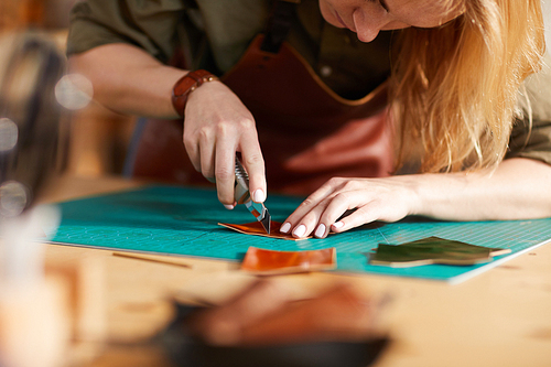 Warm toned close up of young female artisan making leather bag in workshop, copy space