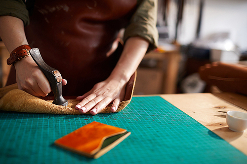 Warm toned close up of female artisan making leather bag in leatherworking atelier, copy space