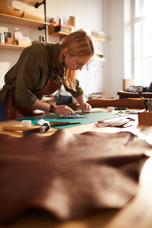 Warm toned portrait of female artisan in leatherworking atelier lit by sunlight, copy space