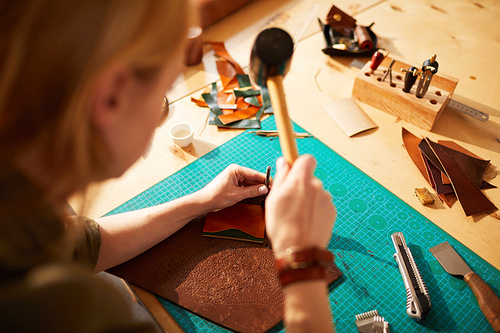 High angle portrait of female artisan making leather bag in leatherworking atelier lit by sunlight, copy space