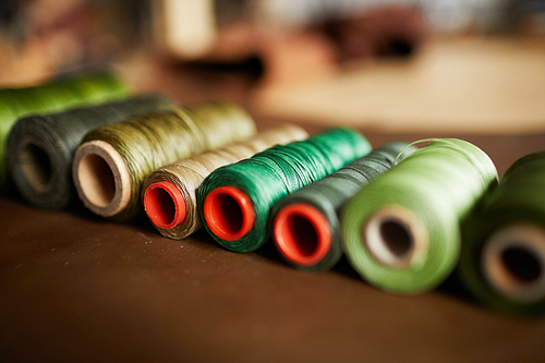 Close up shot of green thread spools lying in textiles in atelier, copy space