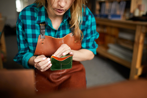 Mid section portrait of female artisan sewing leather wallet in workshop, copy space