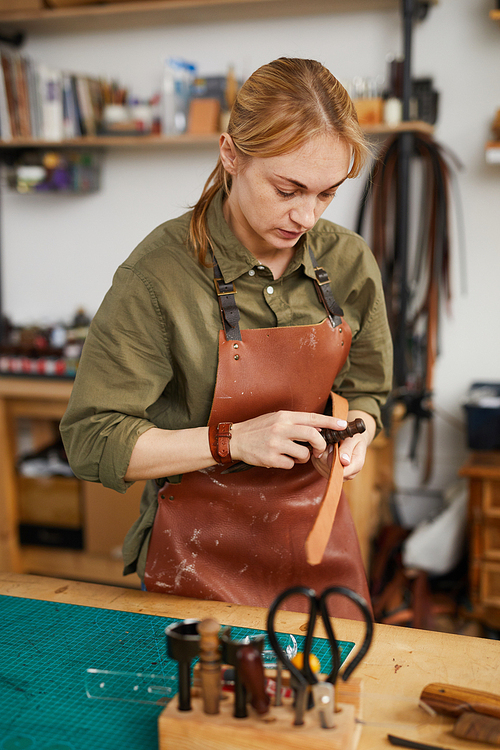 Warm toned waist up portrait of female craftsman working with leather in tannery shop, copy space