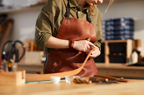 Mid section portrait of female craftsman working with leather in tannery shop, copy space