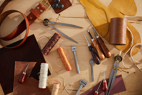 Top view background of tools scattered on wooden table in leatherworking shop, copy space