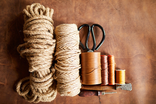 Top view background of various threads and ropes lying on real leather in leatherworking shop, copy space