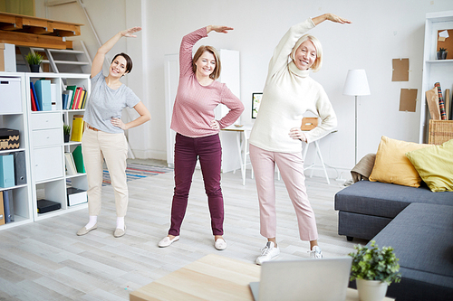 Full length portrait of three adult women stretching during workout at home, copy space